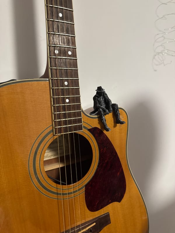 Detailed 3D-printed figurine posed across guitar and printer
