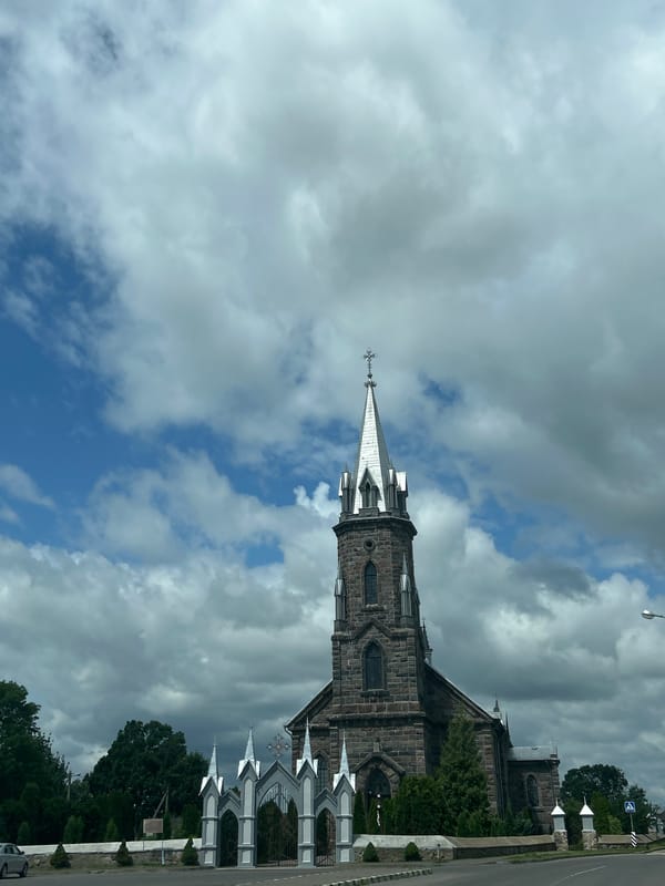 Stone church with pointed spire behind ornate gates, rural Belarus