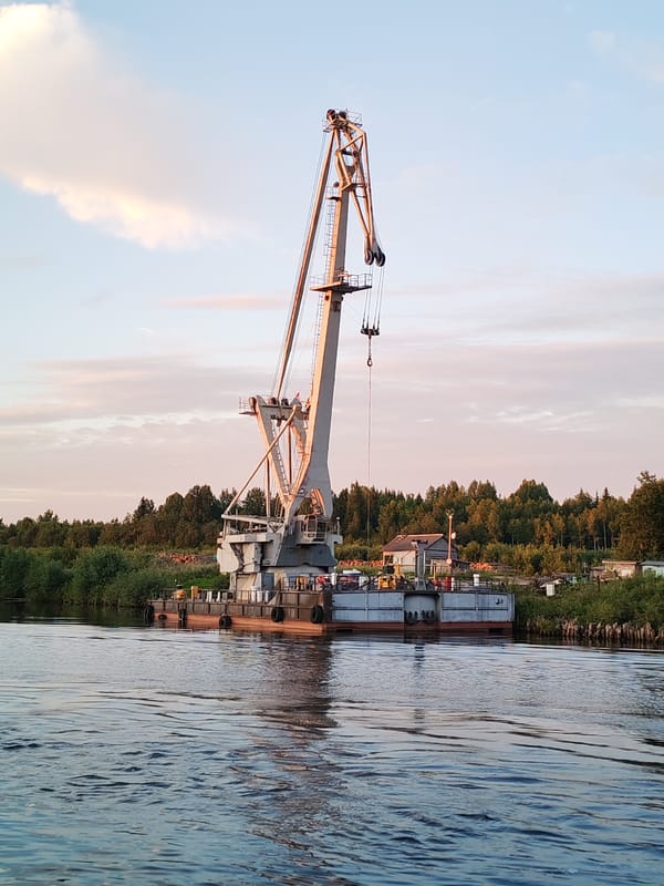Cargo ships and crane barges move through Annensky Most at dusk