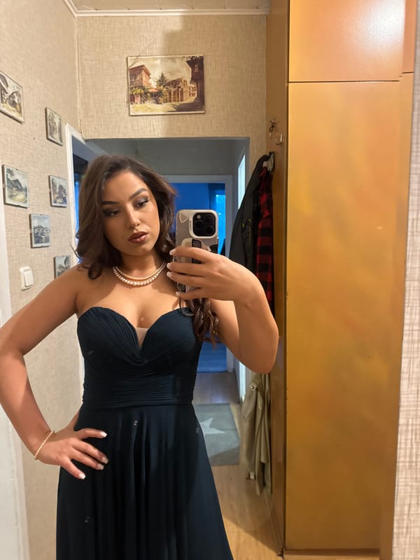 Woman photographs herself in formal green dress and pearls