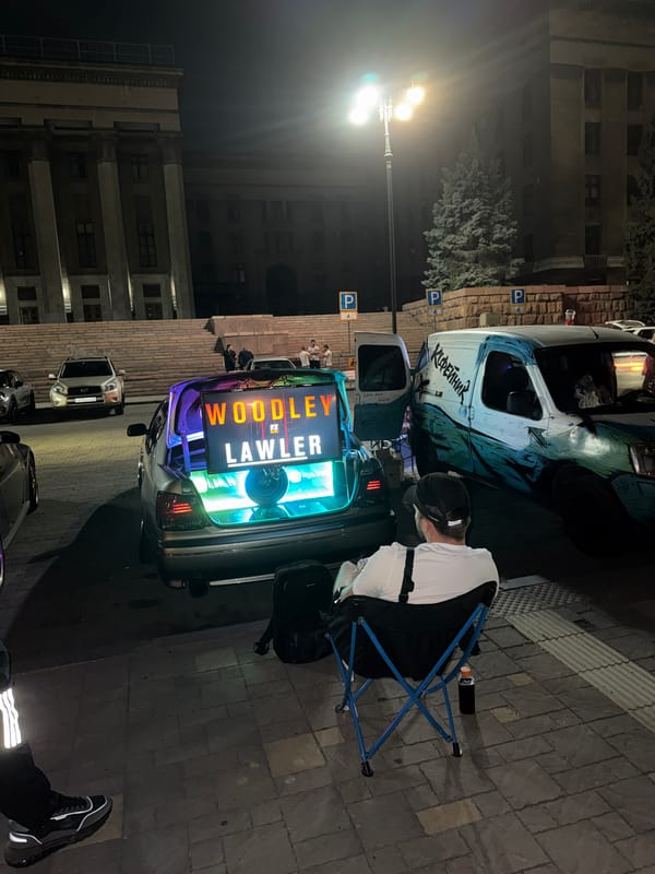 Late-night square hangout with dogs, coffee, and a trunk gaming setup