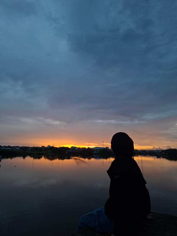 Person enjoys sunset moment with kitten at Lhokseumawe waterfront