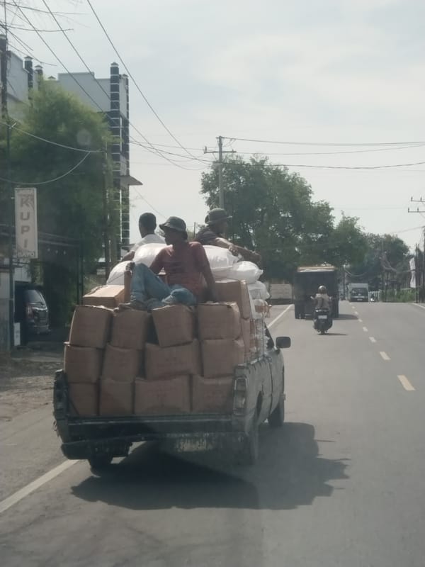 Loaded truck carries three passengers atop cargo in Indonesia