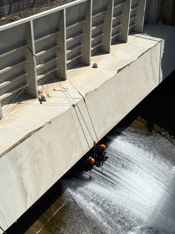 Two helmeted people suspended near dam structure in La Saulce