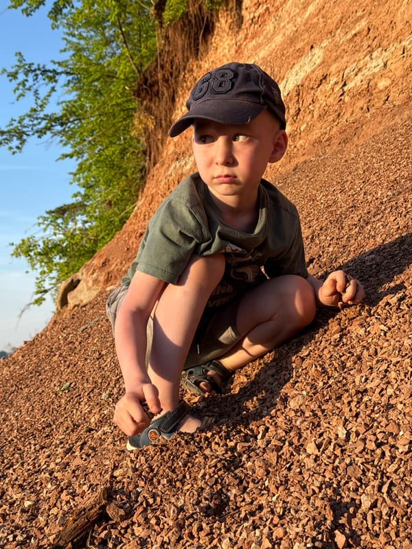 Child sits on gravel holding object in Chaikovsky