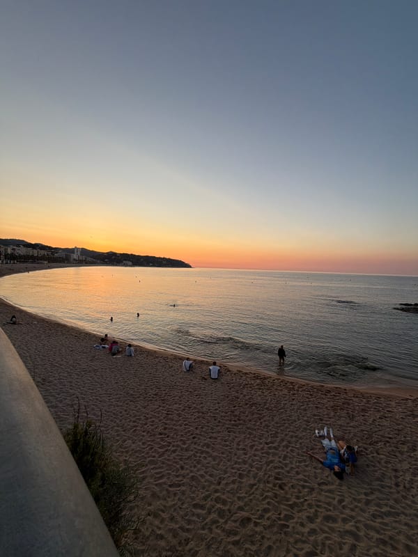 Calm beach at sunset with rocky coastline and scattered figures