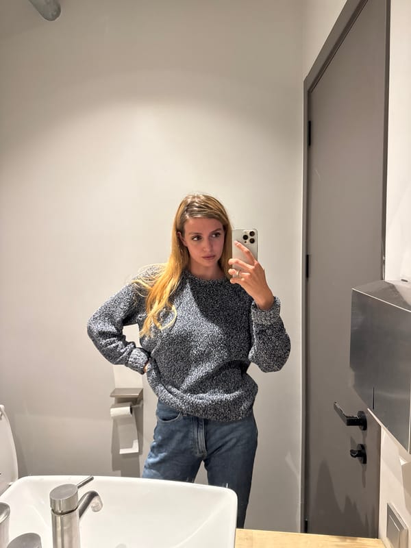 Woman takes bathroom mirror selfies in blue sweater