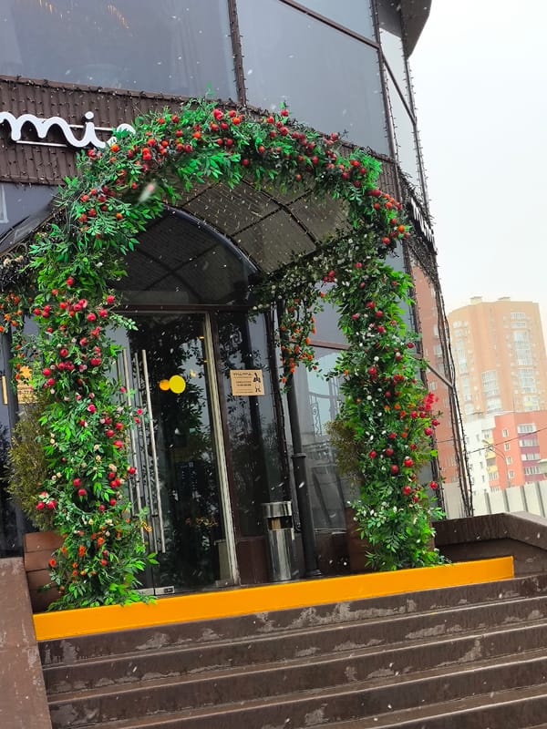 Commercial building entrance with decorative greenery archway documented