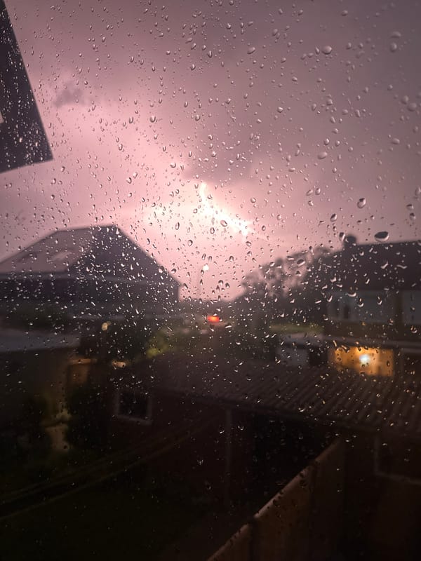 Lightning and rain sweep through a quiet residential neighborhood at night