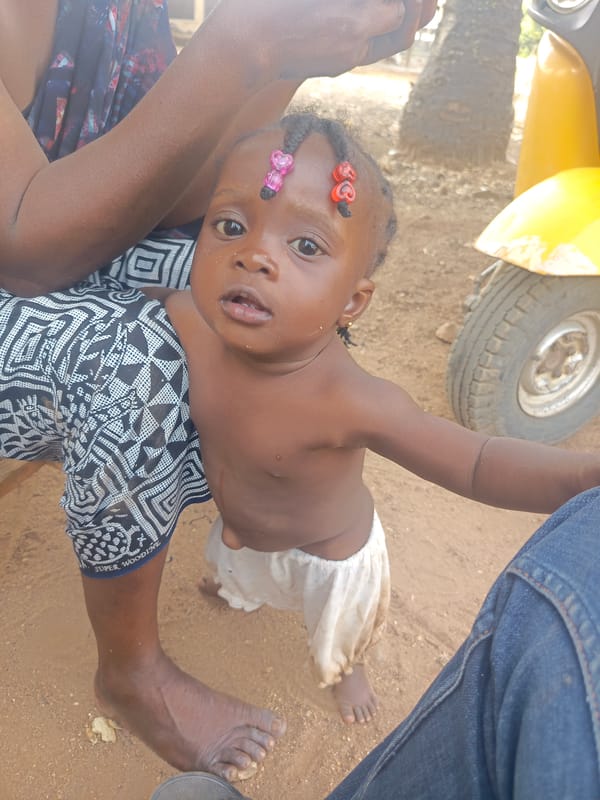 Toddler plays outdoors while woman uses phone in Akwanga