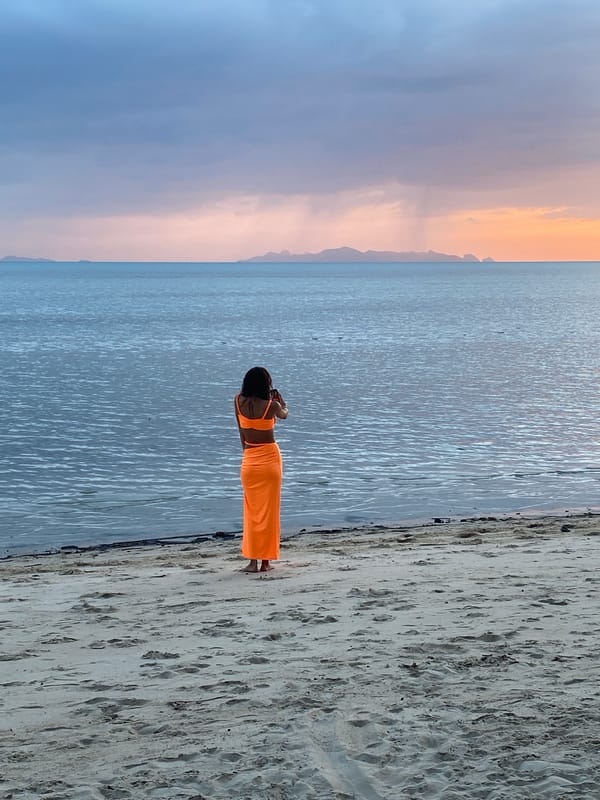 Orange outfit, Ko Samui beach, phone out at the water's edge