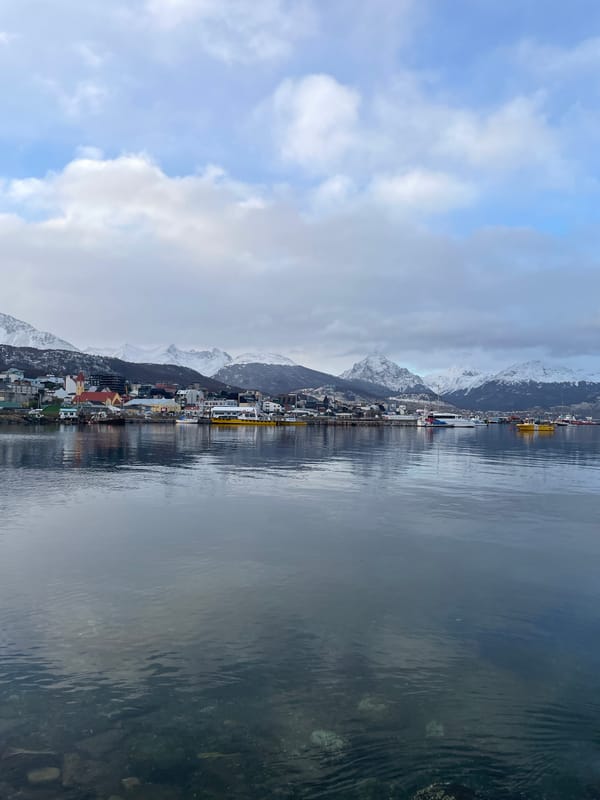 Tourists explore Ushuaia waterfront and memorials under overcast skies