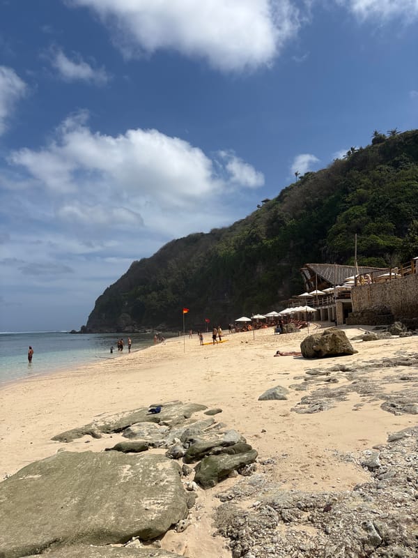 Quiet Kuta Selatan beach, shells on sand, hills behind