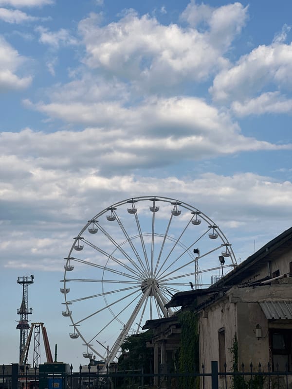 Industrial cranes and a Ferris wheel under a stormy harbor sky