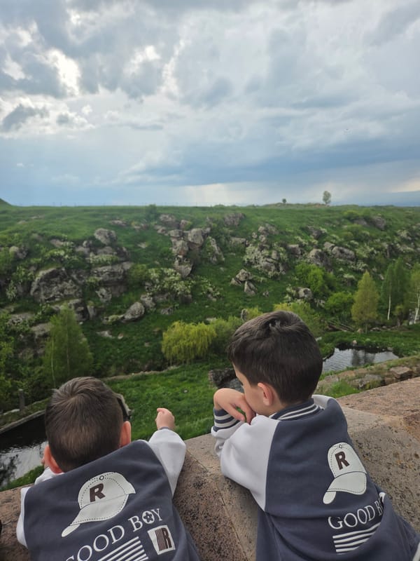 Boys explore historic Armenian monastery grounds amid valley landscape