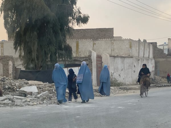 Three covered women walk Kandahar street under overcast sky