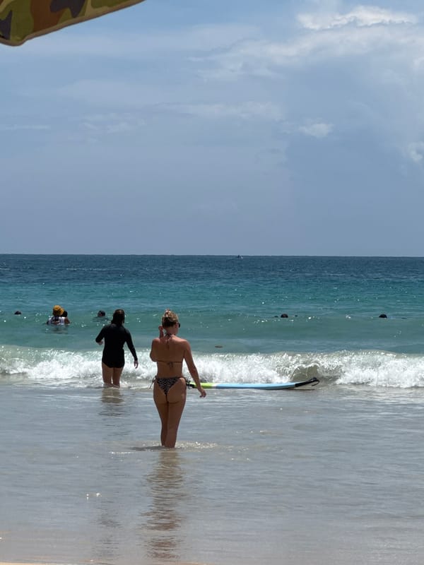 Calm morning at Karon Beach with surfers wading in.