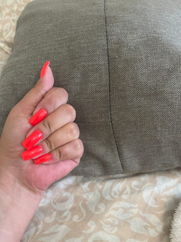 Person displays neon orange square nails on gray fabric