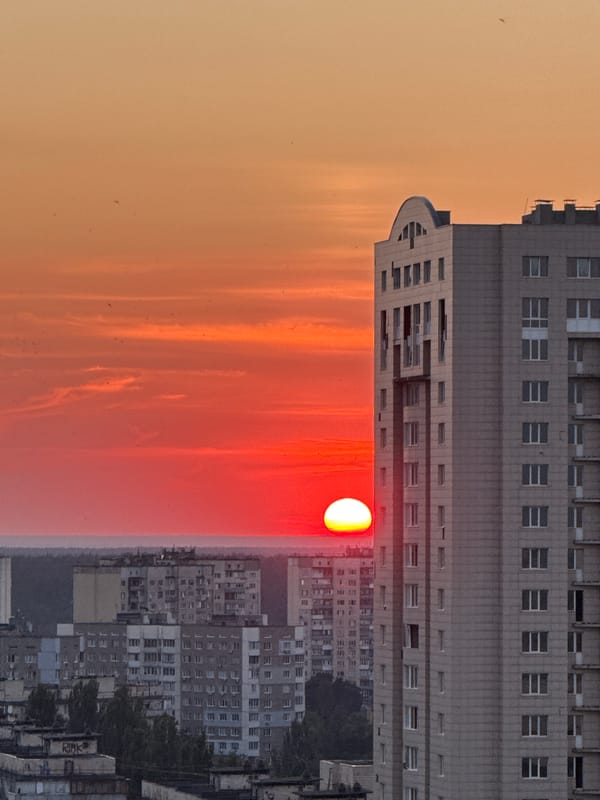City skyline at sunset, sun half-hidden behind apartment tower