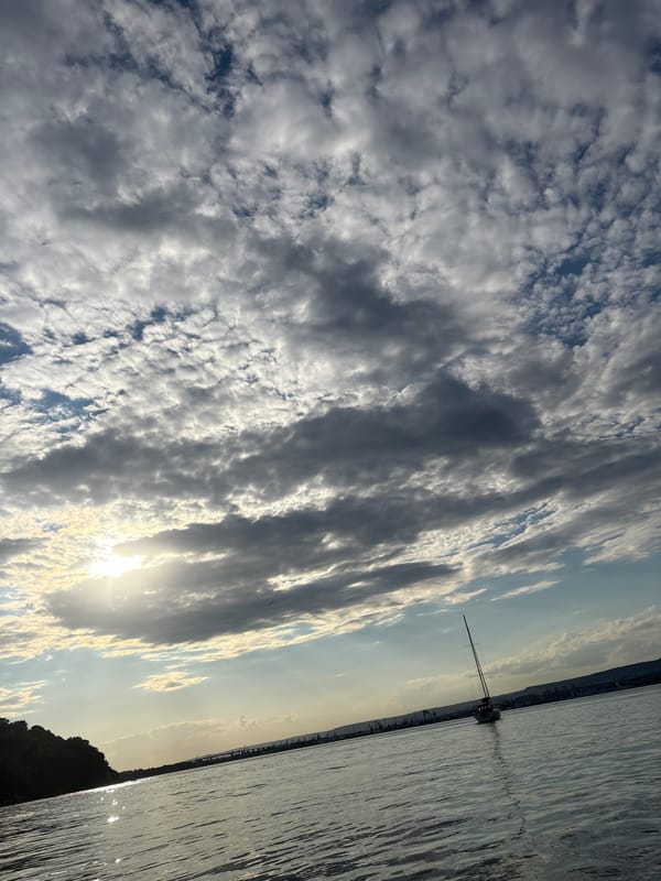Sailboat on green water under a dramatic, cloud-broken sky