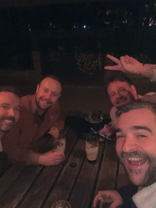 Four men pose for nighttime selfie around outdoor table