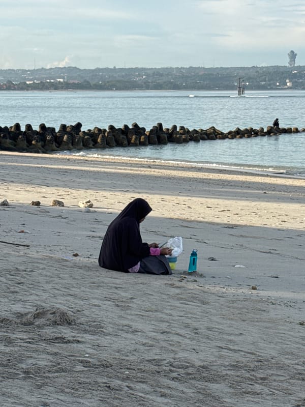 Woman sits on protected Kuta beach holding white object
