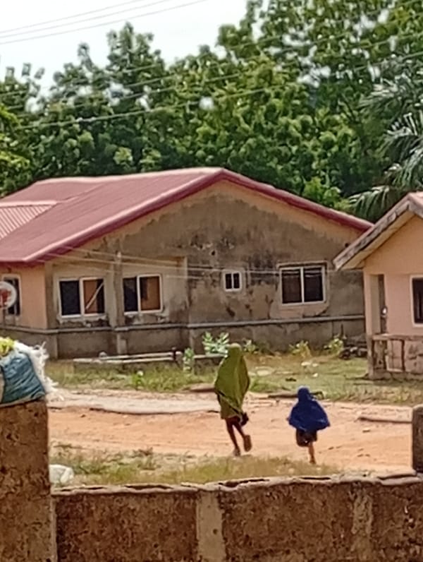 Two robed figures run across dirt field near building