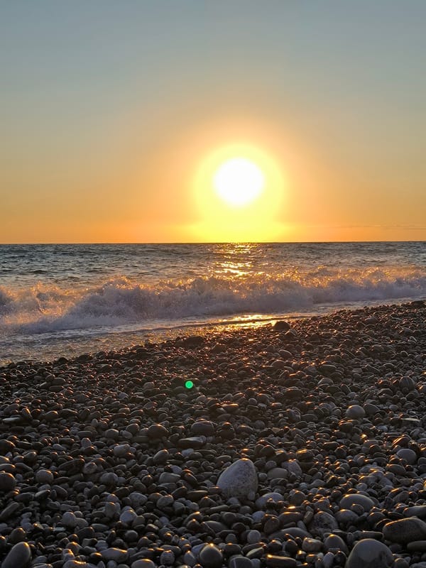 Sunset over Sochi's pebble beach, sea calm and golden