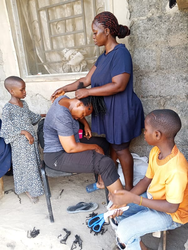 Woman braids hair of seated friend outside building