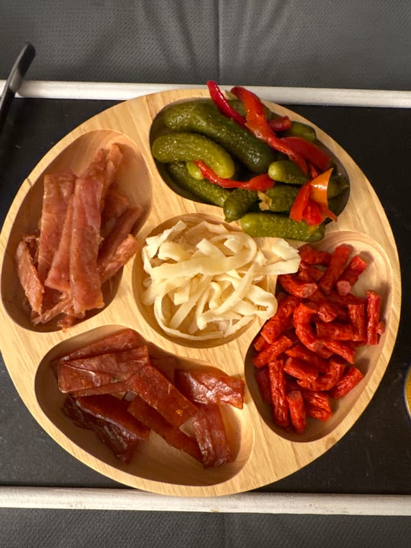 Sectioned wooden food tray with pickles and sausages documented