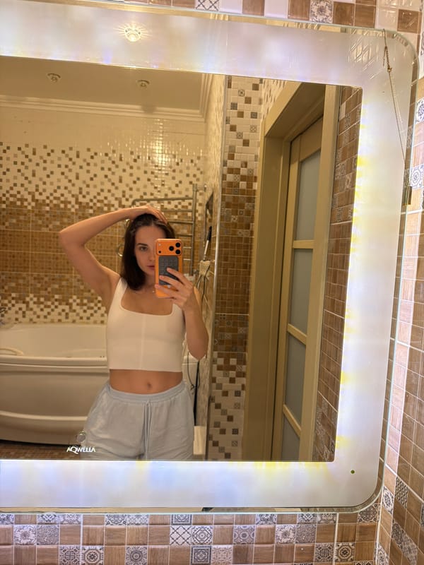 Bathroom mirror selfie in white top and light blue shorts