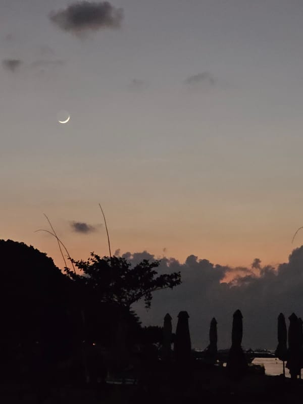 Sanur Beach at dusk: boats, a glowing gazebo, and twilight skies