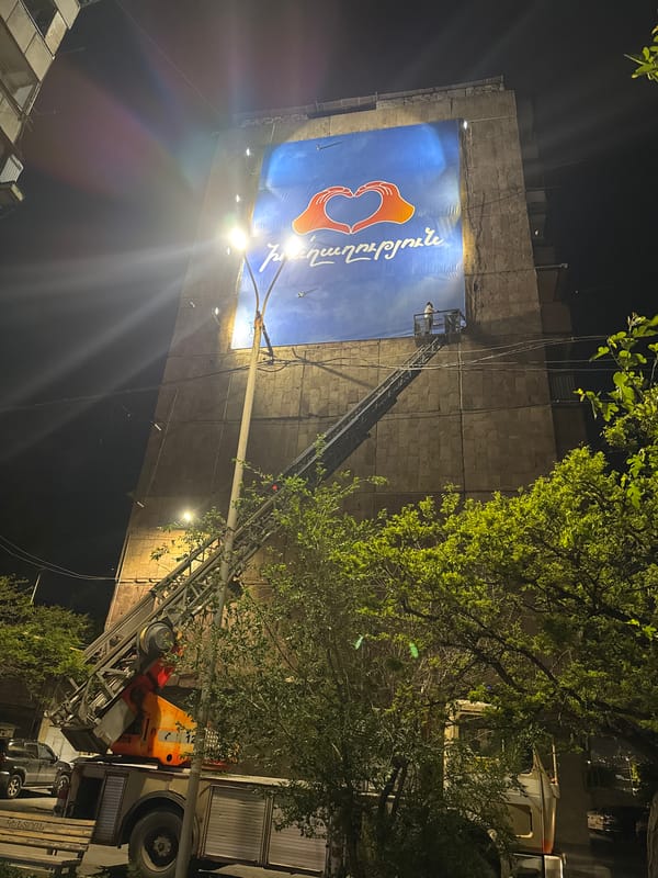 Workers install heart-logo banner on Yerevan building at night