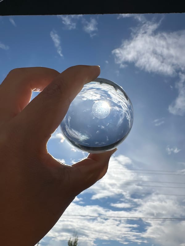 Person photographed with crystal ball against cloudy sky