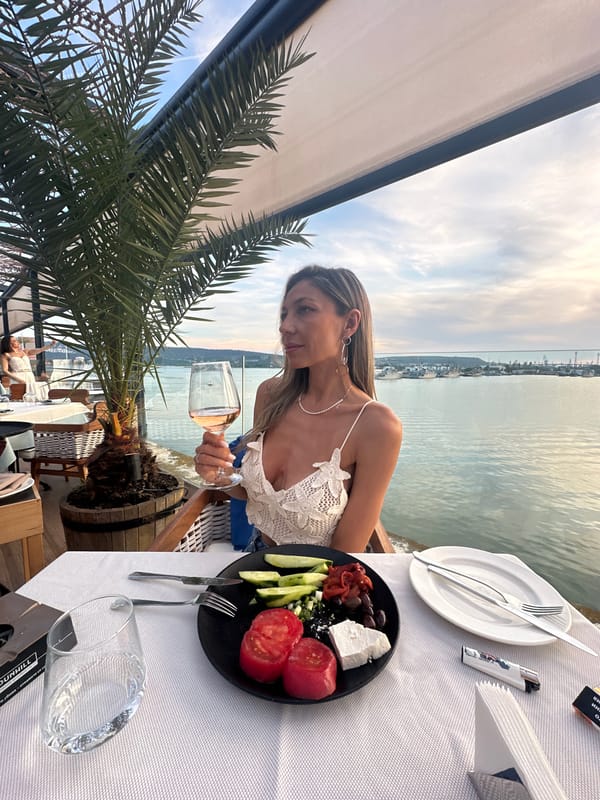 Woman dines waterside with rosé wine and tomatoes