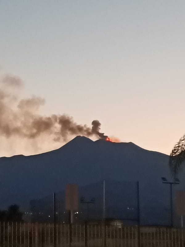 Volcano erupts at dusk, lava glowing above a nearby urban area