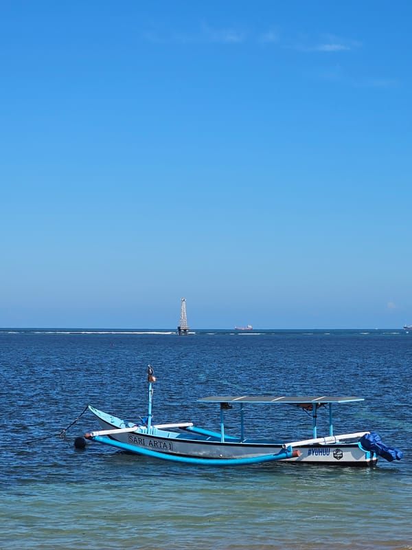 Quiet morning at Sanur Beach, boats, shade trees, and calm water.