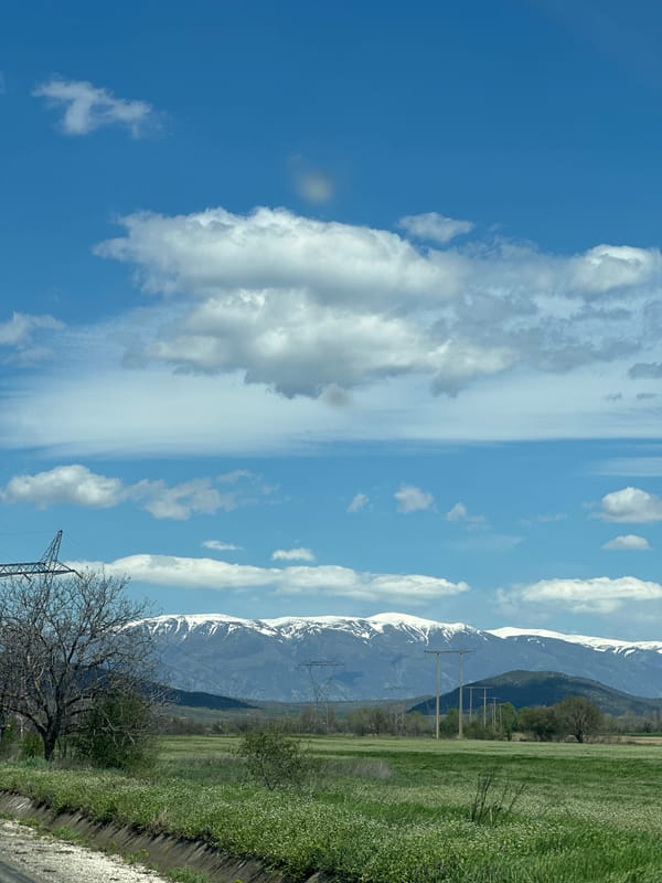Car travels rural road near snow-capped mountains in Bulgaria