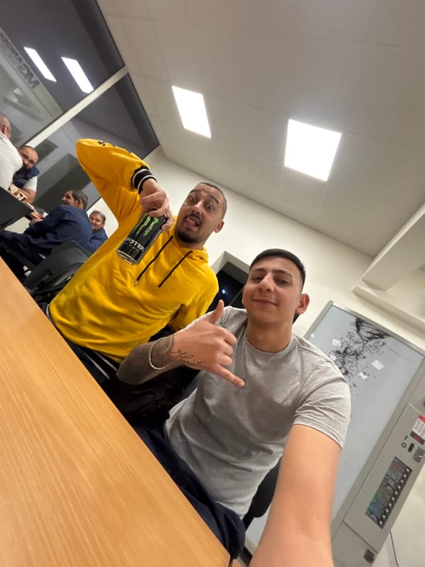 Two men pose for selfie indoors with energy drink
