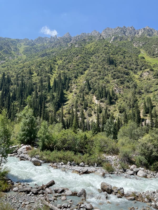 Horseback riders and glacial river in a Kyrgyz mountain valley
