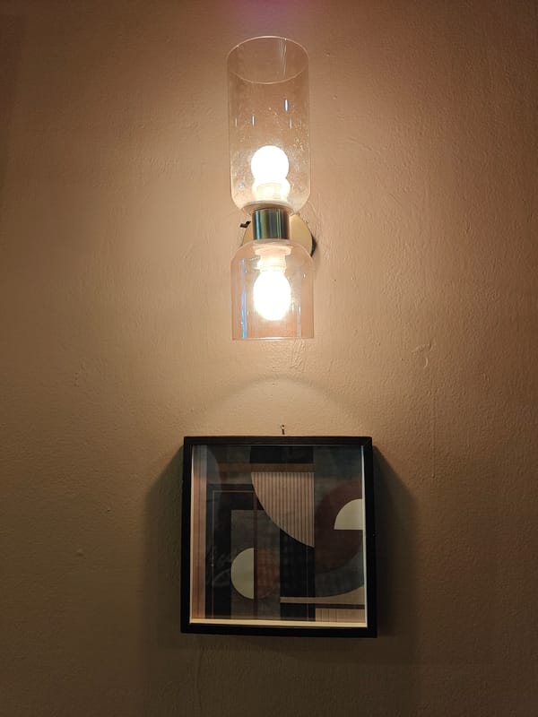 Modern dual-cylinder light fixture observed above artwork in Mumbai