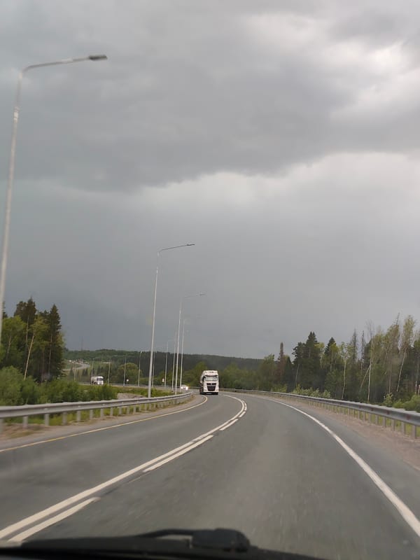 White truck travels forest road in Chusovskoye under cloudy skies