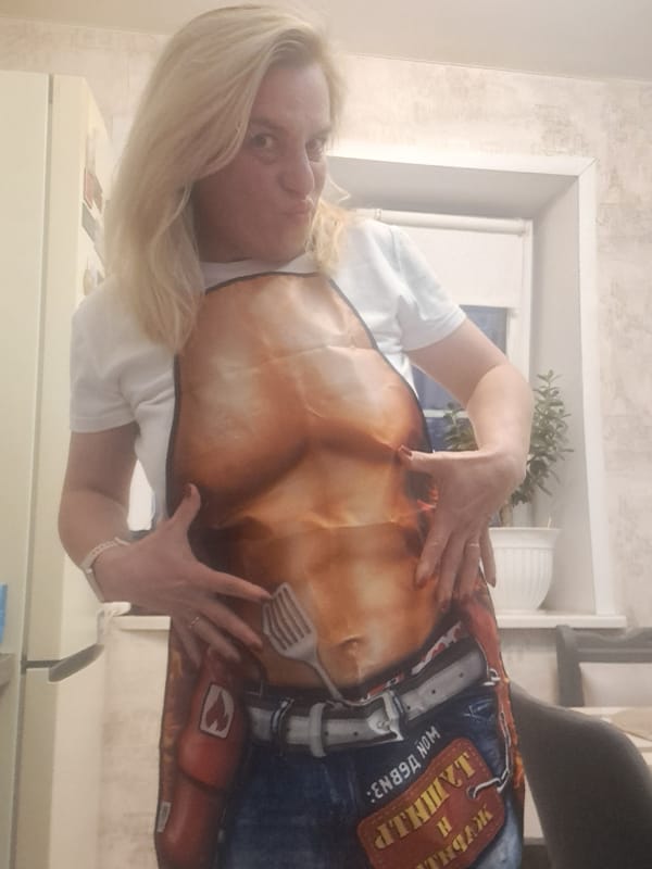 Woman poses with novelty torso apron in Russian kitchen