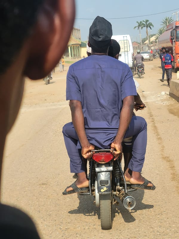 Motorcycle riders travel dirt road near Keffi college