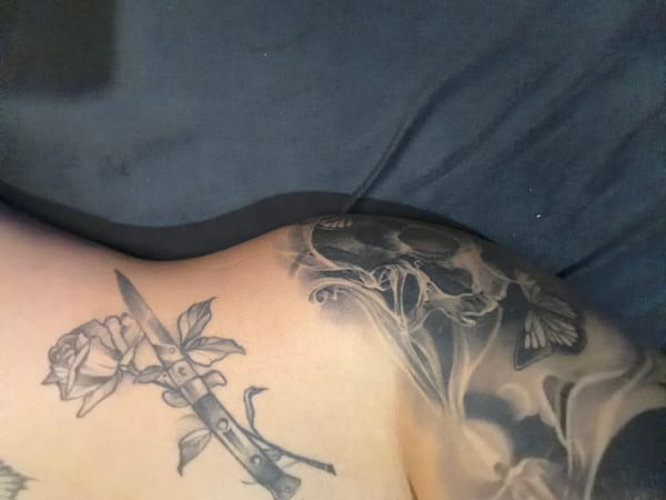 Person displays multiple black ink tattoos including skull butterfly rose