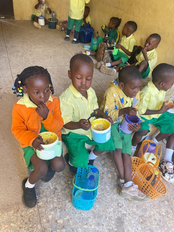 Schoolchildren eat lunch outdoors in Akwanga schoolyard