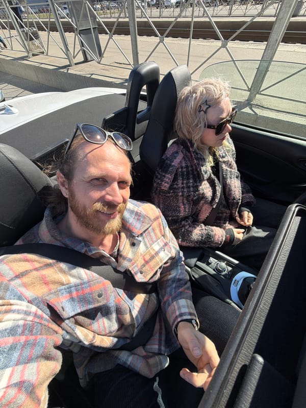 Two people enjoy sunny day in convertible near structure