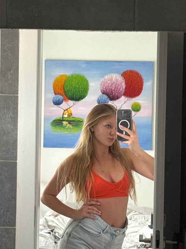 Woman takes mirror selfie in orange top in Ariel