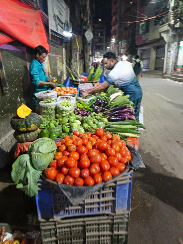 Evening vegetable vendors work Dhaka streets near pharmacy