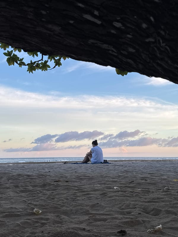 Person sits on Nusa Dua beach under cloudy skies